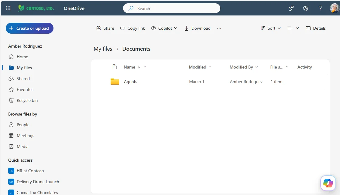 OneDrive web with the new prominent floating Copilot button visible in the bottom-right of an empty Documents view — a pink/purple gradient circle with the Copilot chat-bubble icon